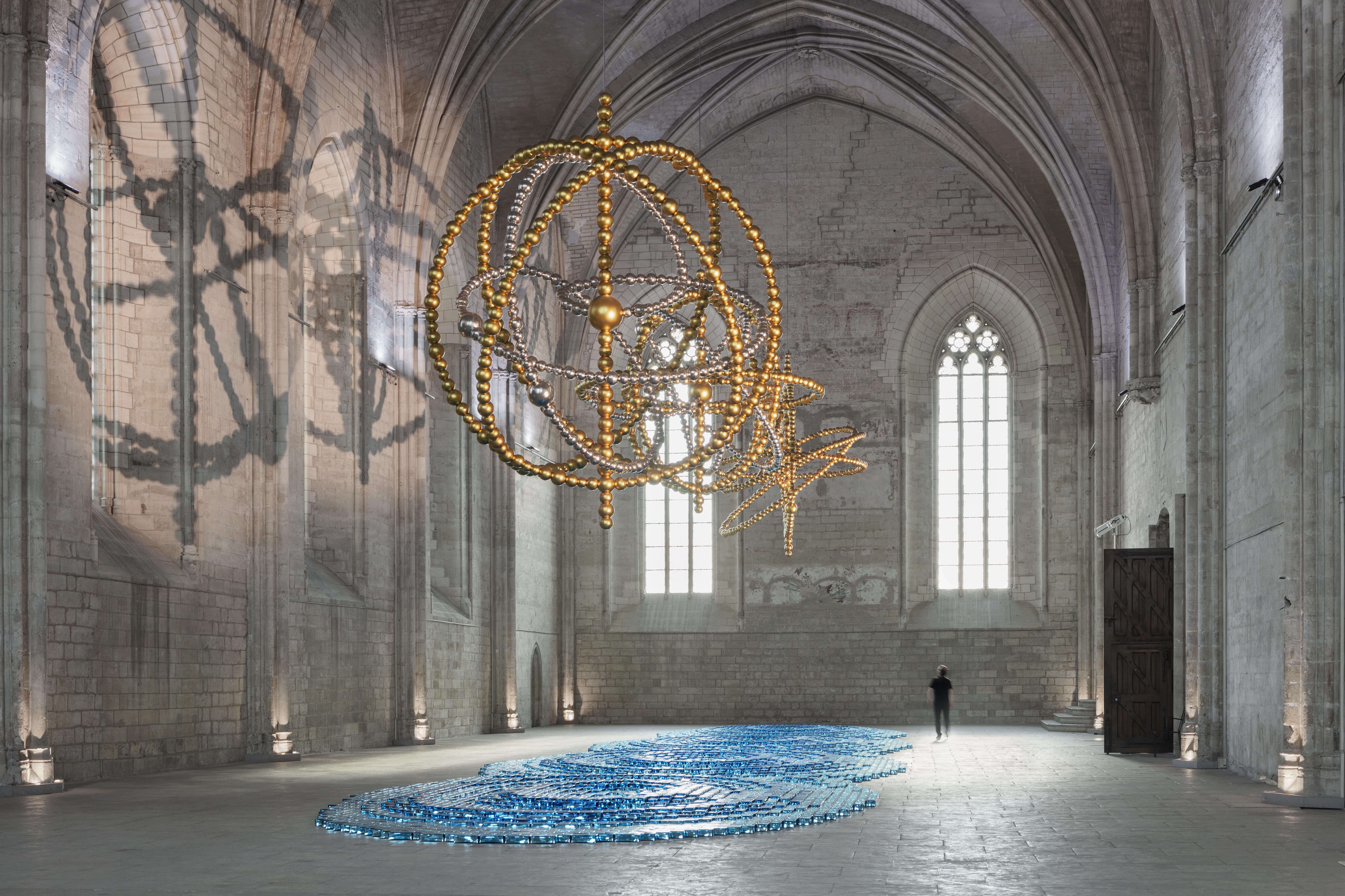 鏡面玻璃珠雕塑垂掛於教堂空間，與地面裝置交織光影與尺度的層次節奏。© Tanguy Beurdeley / Perrotin